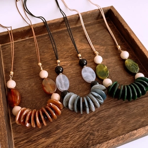 Detail of vintage bohemian resin long necklaces in earthy tones on a rustic wooden tray