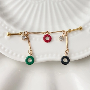 Macro shot of gold ear piercing bar with red, green and black drip glaze rings