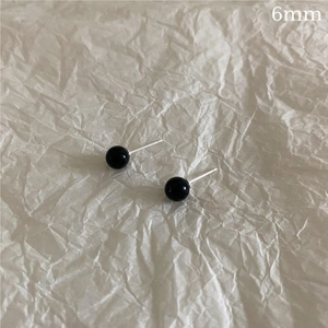 Close-up of 6mm black agate stud earrings on textured paper with silver needle detail