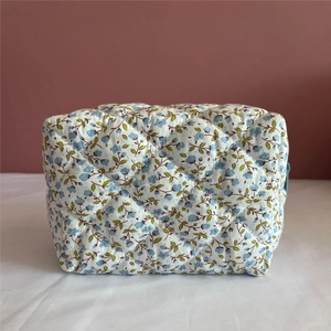 Detail of blue floral quilted makeup bag featuring a blue zipper and cotton texture
