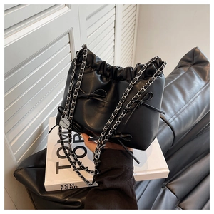 Close-up of black drawstring bucket bag with decorative bows and silver chain strap