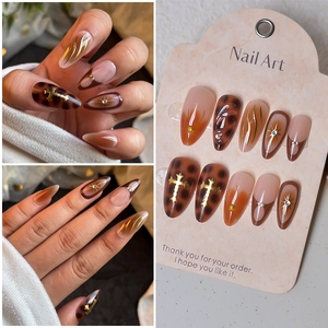 Macro detail of amber tortoiseshell press-on nails with golden cross and star rhinestones