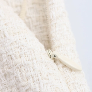 Detail view of cream tweed fabric texture with a high-quality invisible zipper and metal slider