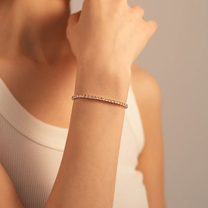 Detailed close-up of a gold tennis bracelet with tiny clear zircons on a model wrist