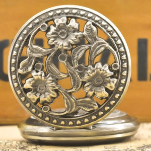 Close-up of vintage bronze pocket watch with hollow floral pattern and heart detail