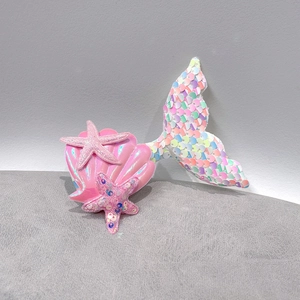 Close-up of sequined mermaid tail, pink shell, and glitter starfish hair accessories