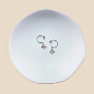 Macro view of silver butterfly nipple rings with zircon on a white ceramic tray
