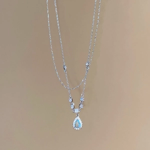 Detail of silver chain necklace featuring a blue waterdrop pendant with inlaid crystals