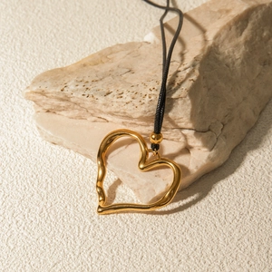 Detail of 18k gold plated heart pendant with wax cord on a textured stone background