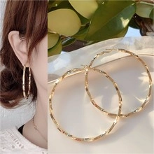 Detailed close-up of large golden hoop earrings with unique spiral texture on model