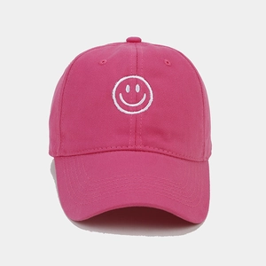 Detailed view of white smiley face embroidery on bright pink cotton baseball cap