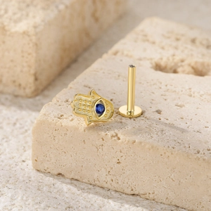 Macro view of gold Hamsa Hand ear stud with blue evil eye stone on stone surface