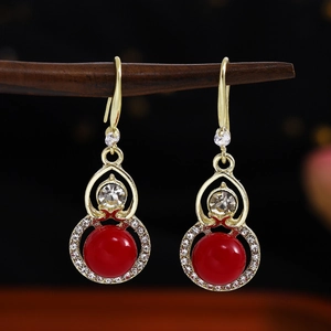 Detail of red beaded earrings with white rhinestones hanging on a wooden stand