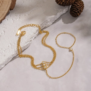 Detail of 18K gold-plated hand chain with three white zircons on a rustic stone background
