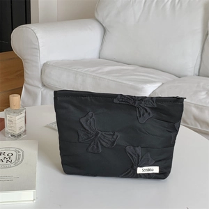 Close-up of black butterfly embroidered makeup bag with Sozakka label on white table