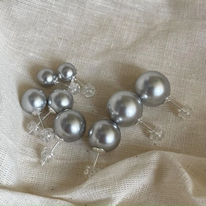 Macro view of silver gray pearl earrings in multiple sizes on textured fabric background