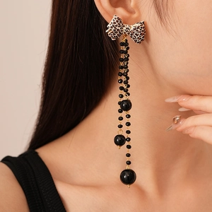 Detailed view of leopard print bow earrings with long black beaded tassels and gold finish