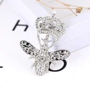 Gros plan détaillé d'une broche abeille argentée avec motif couronne, cristaux et perle