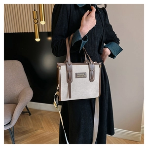 Detail of canvas tote bag with contrast leather handles shown by model in minimalist setting