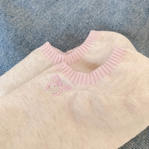 Detailed view of beige no-show socks with pink ribbing and embroidered bow on denim background