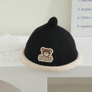 Detail of knitted baby hat featuring cute bear patch and soft black and white texture
