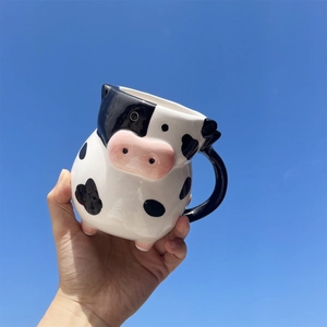 Detail of a 3D cow shaped ceramic coffee mug with black spots held against a clear blue sky