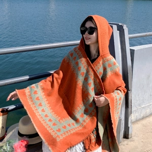 Gros plan du poncho à capuche orange avec motifs cœurs tricotés et détails de franges