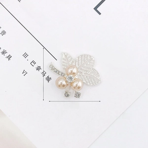 Spilla in lega di zinco con perle color champagne e zirconi su sfondo bianco pulito