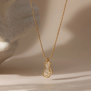 Detail of a gold cat pendant with micro-paved crystals on a polished ball chain necklace