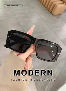 Detail of hand-held black rectangle sunglasses with thick frames and dark gradient lenses