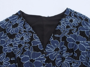 Détail du col en V avec broderie florale 3D en denim bleu sur un tissu noir chic