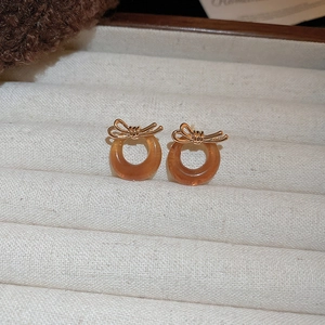 Detail of amber-toned resin earrings with golden bow accents on soft velvet display