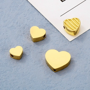 Dettaglio di quattro perline in metallo dorato a forma di cuore con fori per creazione gioielli