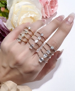Detailed view of silver rings with emerald and round cut moissanite on female hand