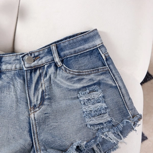 Detailed macro view of distressed denim shorts with ripped holes and button waist