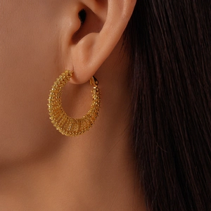 Detail of gold beaded hoop earring showing intricate woven metal mesh on a model
