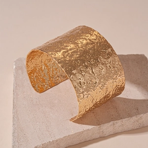 Macro detail of the hammered texture and golden metallic finish on the wide cuff bracelet
