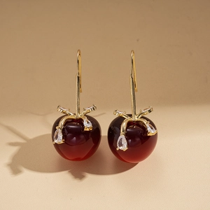 Détail de boucles d'oreilles cerises rouges avec tiges dorées et feuilles en strass
