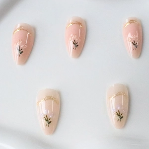 Almond-shaped press-on nails with 3D floral designs and gold foil on nude pink base