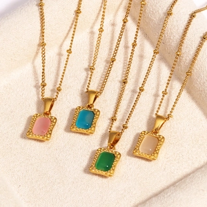 Detail van vier gouden kettingen met vierkante hangers in roze, blauw, groen en crèmewit