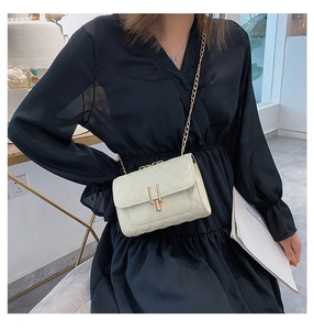 Close-up of beige quilted chain bag with gold metal lock on black dress backdrop