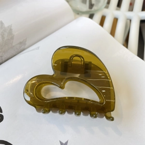 Gros plan d'une pince à cheveux en résine vert olive en forme de cœur sur un livre blanc
