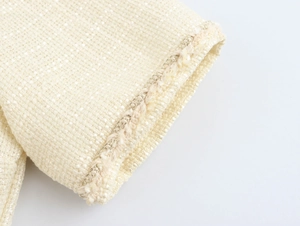 Gros plan d'une manche en tweed beige avec des franges et des fils de soie dorés