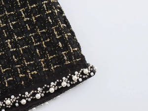 Dettaglio ravvicinato del tessuto tweed nero e oro con eleganti perline e perle