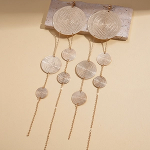 Close-up of textured golden metal earrings with layered round discs and long tassels