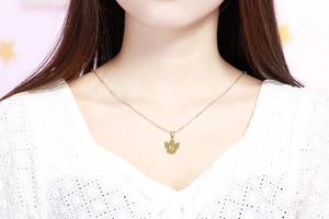 Dettaglio di una collana in acciaio dorato con ciondolo lettera G su camicetta bianca
