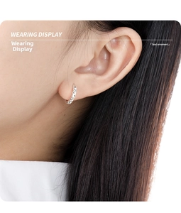 Macro view of a geometric diamond-cut silver hoop earring shown on a model's ear lobe