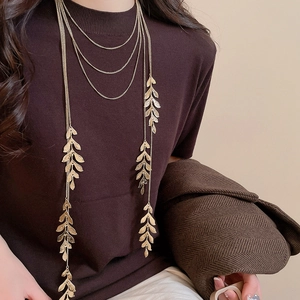 Close-up of a layered gold leaf pendant necklace worn on a brown knit sweater