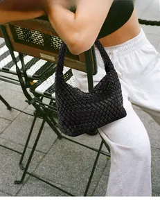 Detailed view of a hand-woven black leather hobo bag held by a model in an outdoor setting