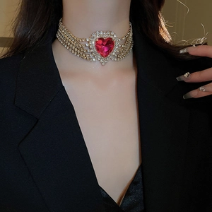 Close-up of gold layered diamond necklace with a striking red heart-shaped gemstone pendant